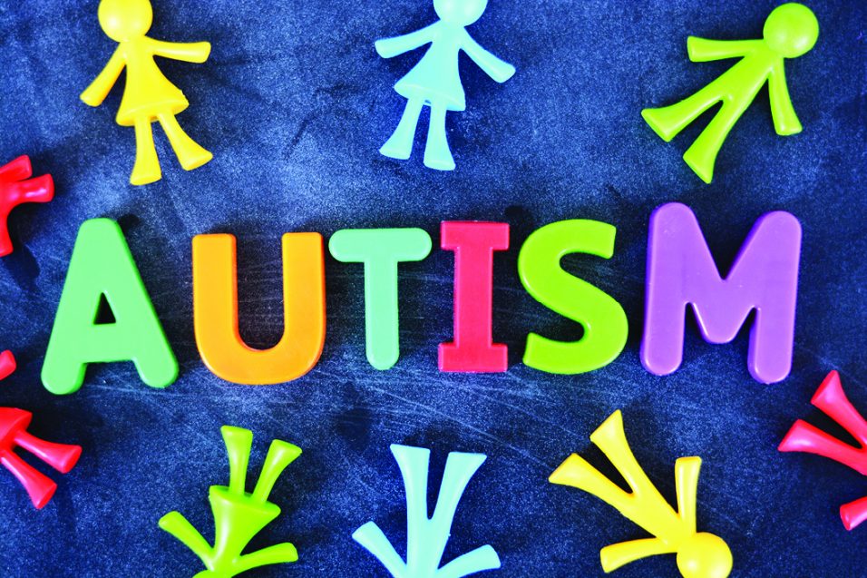 Autism word spelled in colored letter blocks with colorful human miniature on dark background