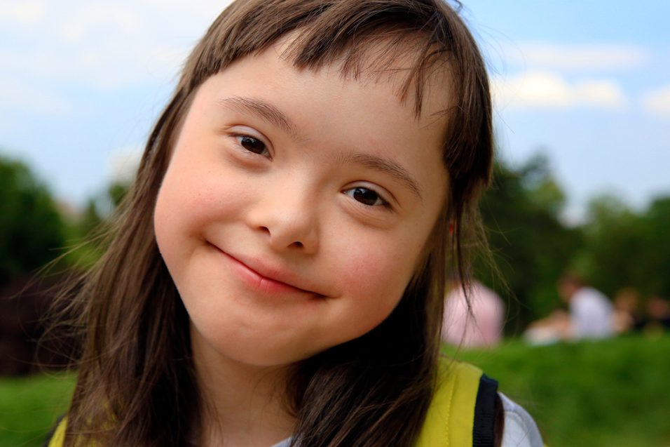 A young girl with Down syndrome smiling outside