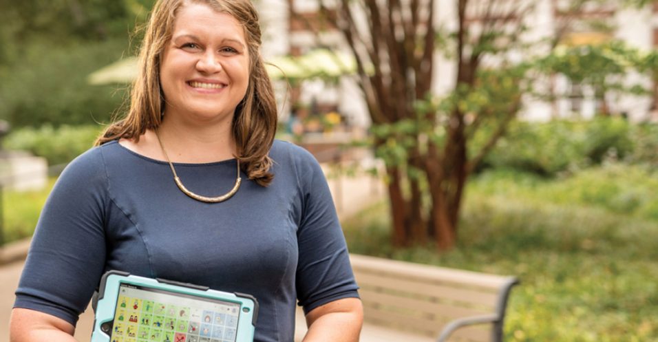 Elizabeth Biggs standing outside holding AAC device