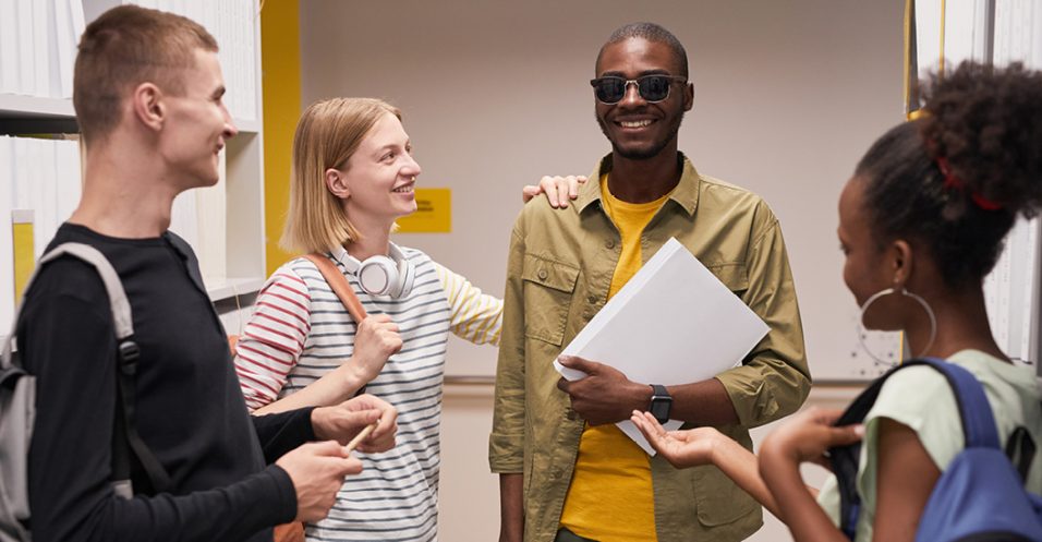 Diverse group of students chatting with smiling blind man