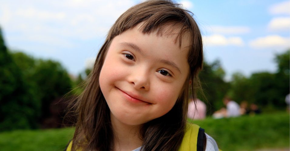 Young girl with Down syndrome smiling outside.