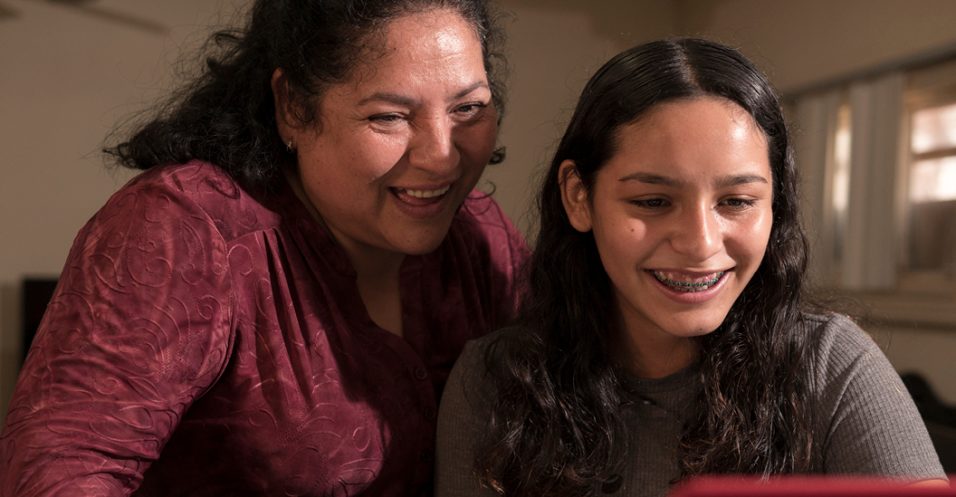 A young adult and her mom smiling while looking at a laptop together.